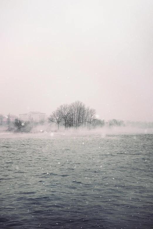 a large body of water with trees in the background, inspired by Elsa Bleda, pexels contest winner, romanticism, snowstorm ::5, white smoke atmosphere, analogue photo low quality, scattered islands