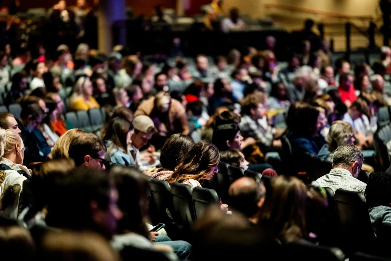 a large group of people sitting in a room, a photo, theater, profile image, colorful crowd, schools