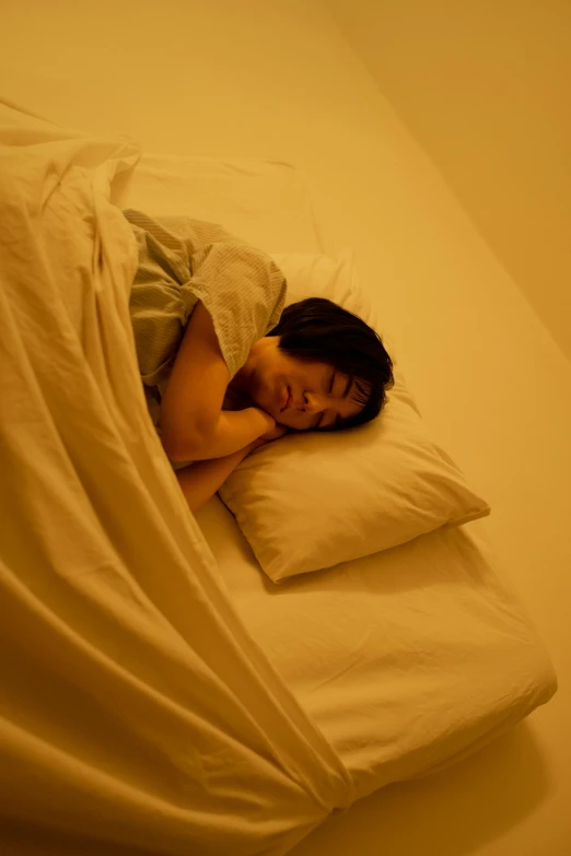 a woman laying on top of a bed covered in sheets, inspired by Elsa Bleda, pexels, yellow hue, japanese, asleep, nighttime