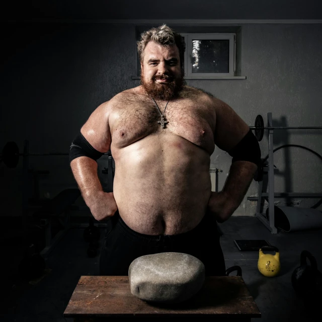 a man standing next to a rock in a gym, by Hallsteinn Sigurðsson, featured on reddit, purism, sumo wrestler, studio portrait, thick mustache, sitting on top a table