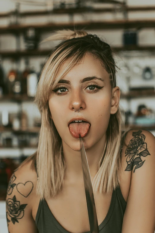 a woman sitting at a table with a knife in her mouth, a tattoo, inspired by Elsa Bleda, trending on pexels, tongue out, drinking at the bar, heart shaped face, blonde crea