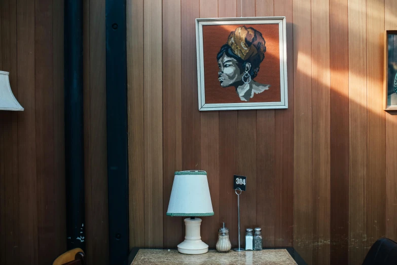 a table topped with a lamp next to a painting, a portrait, unsplash, visual art, at a 5 0 s diner, wood paneling, pompadour, high details photo