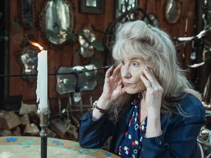 a woman sitting at a table with a candle in front of her, a portrait, inspired by Florence Engelbach, trending on pexels, looking in mirror at older self, kiki smith, cottage hippie naturalist, vivienne westwood