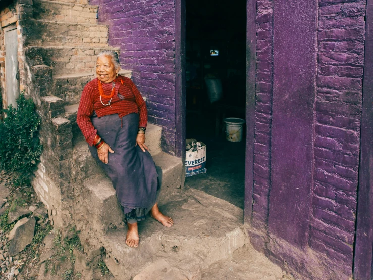 a woman sitting on the steps of a purple building, pexels contest winner, cloisonnism, nepal, grandma, 90s photo, of a full body