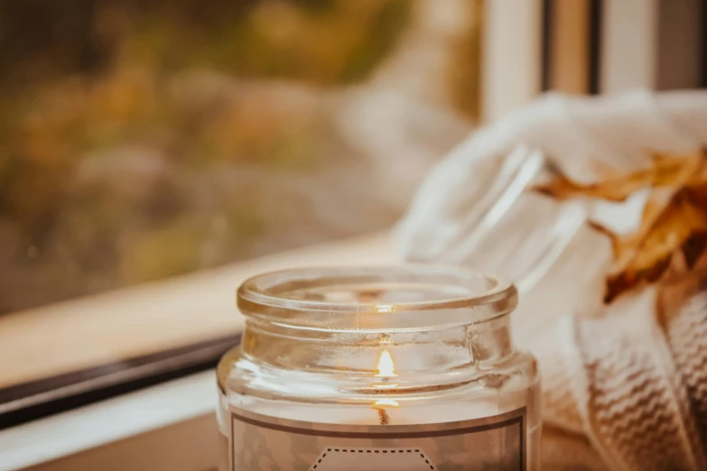 a candle that is sitting on a window sill, by Emma Andijewska, trending on pexels, jar of honey, subtle detailing, cosy, close up angle