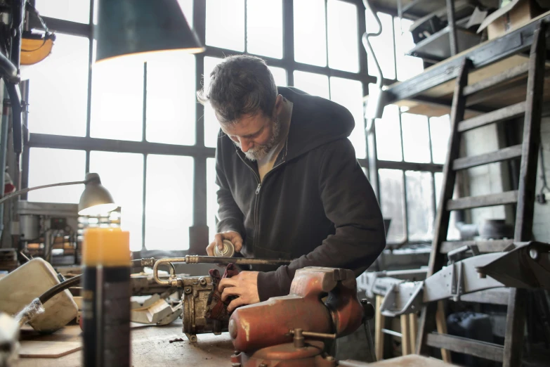 a man working on a piece of wood in a workshop, by Jan Tengnagel, pexels contest winner, arts and crafts movement, carbide lamp, weathering armor plating, deus ex machina, lachlan bailey