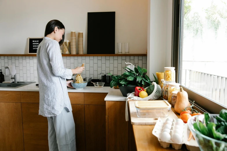 a woman standing in a kitchen preparing food, pexels contest winner, happening, background image, nanae kawahara, standing in corner of room, breakfast