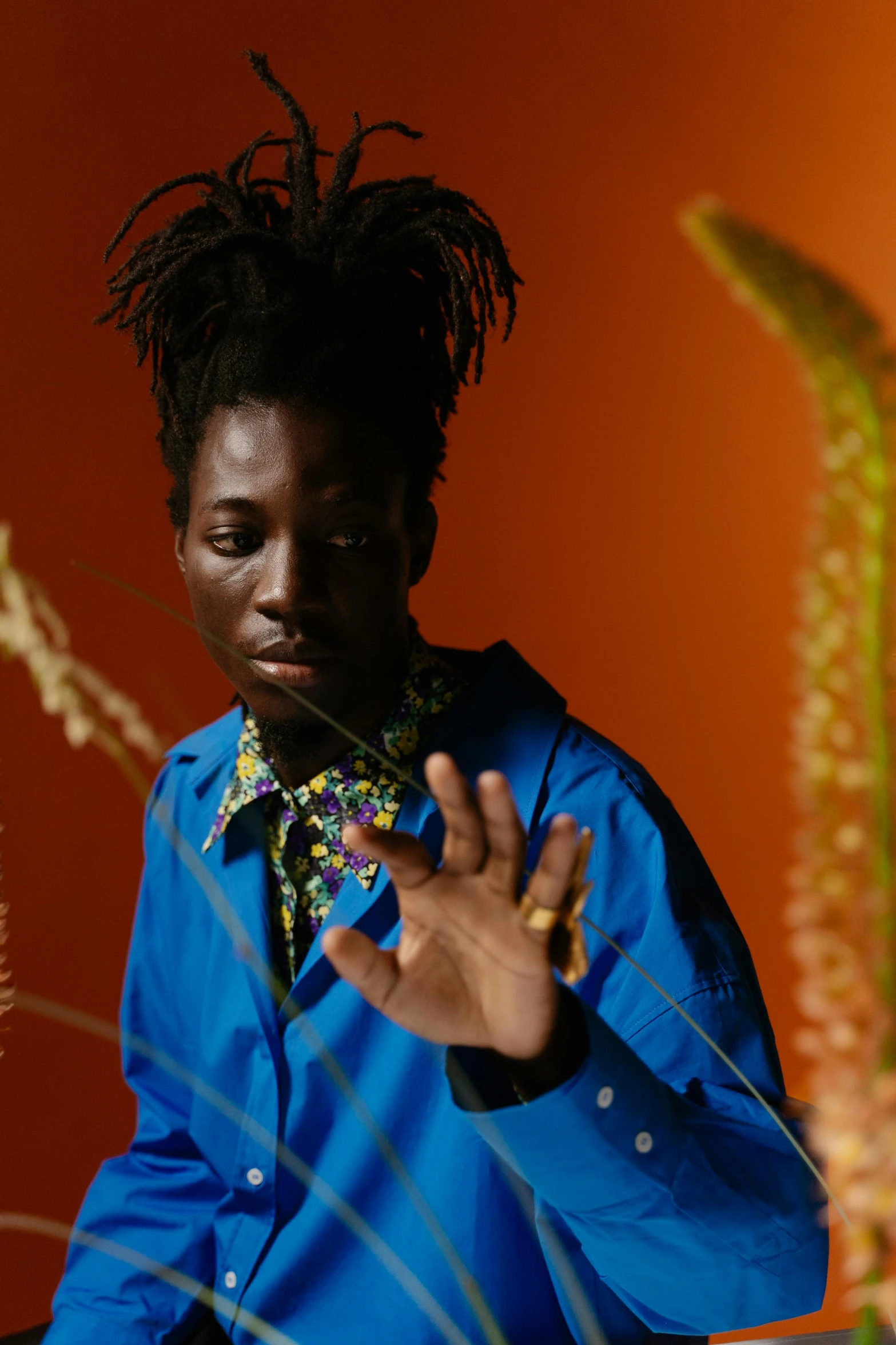 a man with dreadlocks standing in front of a plant, by Nathalie Rattner, trending on pexels, afrofuturism, wearing blue jacket, adut akech, wearing a colorful men's suit, catalog photo