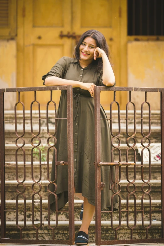 a woman standing in front of a gate talking on a cell phone, a picture, pexels contest winner, idian dress, green and brown clothes, square, at college