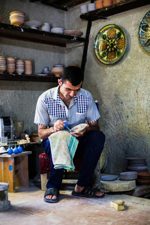 a man that is sitting down in a room, a silk screen, handmade pottery, turkey, working hard, square