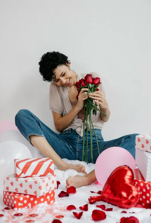 a woman sitting on a bed holding a bouquet of roses, pexels contest winner, party balloons, nathalie emmanuel, red hearts, picking up a flower