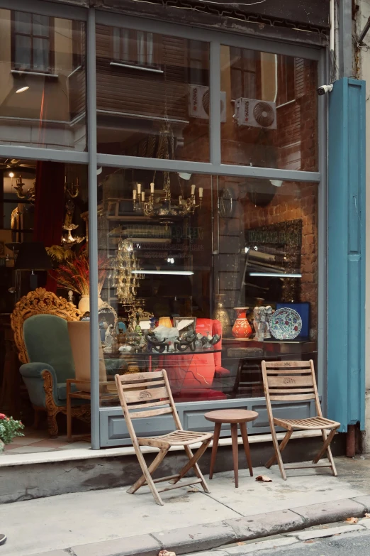 a couple of wooden chairs sitting in front of a store, a photo, arts and crafts movement, eclectic, cosy, glazed, urban surroundings