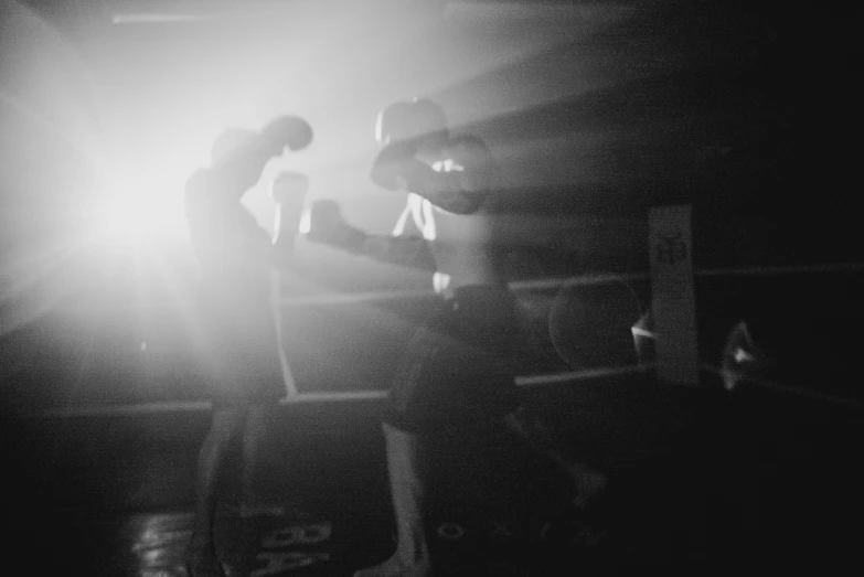 a black and white photo of two boxers in a boxing ring, by Emma Andijewska, unsplash, light coming through, holga 120n, silhouette!!!, night life