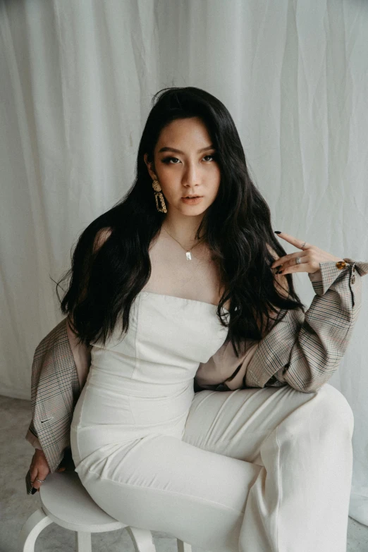 a woman sitting on top of a white chair, an album cover, inspired by Huang Ji, trending on pexels, long wavy black hair, silver，ivory, fashion, clothing