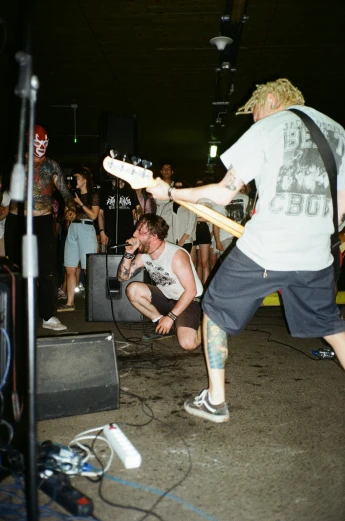 a man standing on top of a stage with a guitar, reddit, lowbrow, gang saints wear yellow bandanas, looking at bloody fist, outside on the ground, analog photo