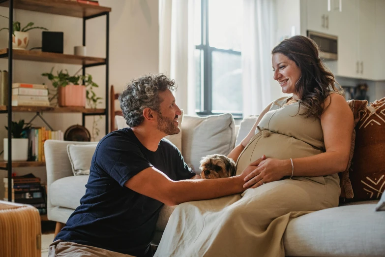 a man and woman sitting on a couch with a dog, pregnant belly, profile image, lachlan bailey, feels good man