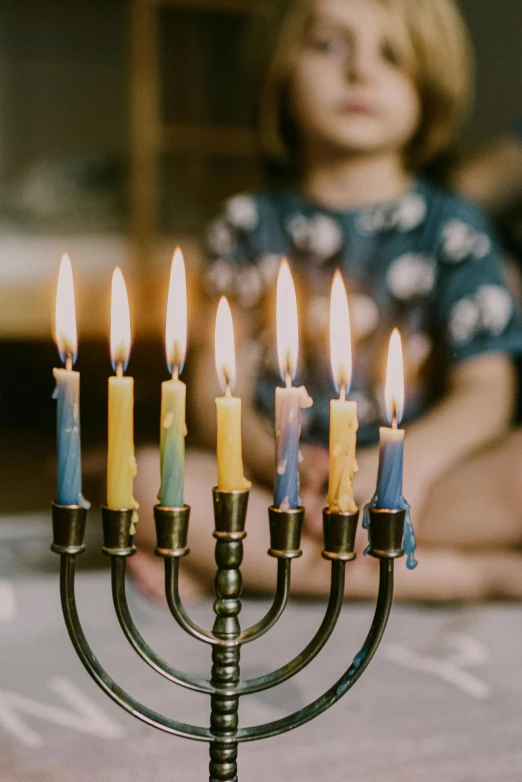 a young girl sitting at a table with a menorah in front of her, trending on unsplash, fine art, zoomed in, happy birthday candles, full frame image, light over boy