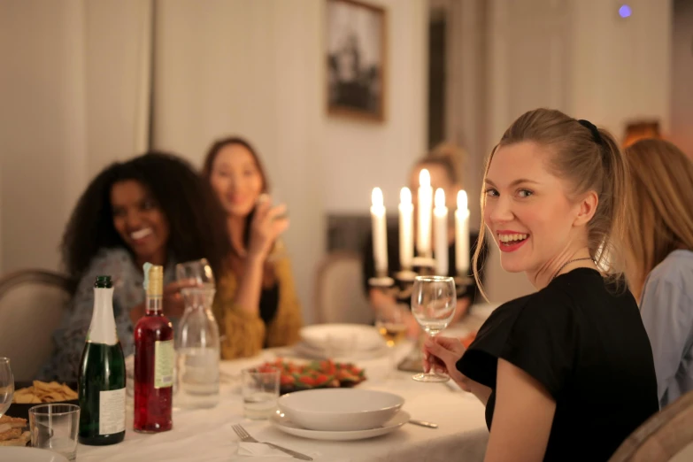 a woman sitting at a table with a glass of wine, a group of people, natural candle lighting, profile image, swedish