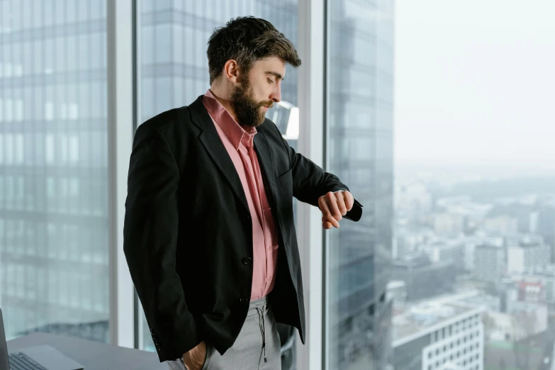 a man standing in front of a window looking at his watch, pexels contest winner, office clothes, with a beard and a black shirt, wearing a pink tux, thumbnail