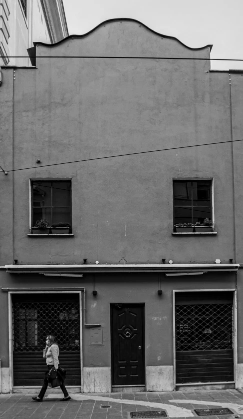 a black and white photo of a person walking in front of a building, a black and white photo, inspired by André Kertész, unsplash, ffffound, wires, warsaw, old house