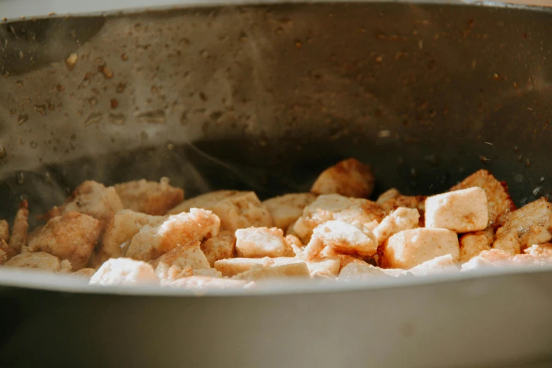 a pan filled with food sitting on top of a stove, by Emma Andijewska, pexels, process art, chicken nuggets, bubbling skin, clay material, creamy