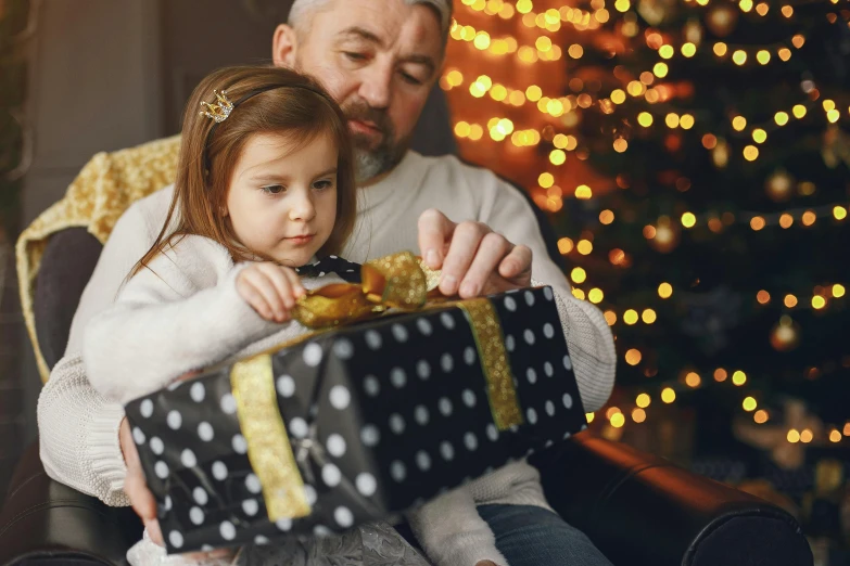 a man holding a little girl in front of a christmas tree, pexels contest winner, holding gift, square, avatar image, girls