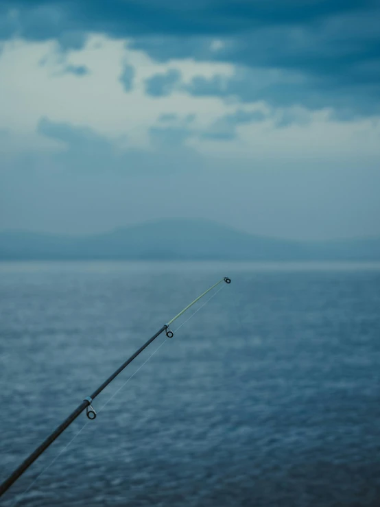 a fishing rod sitting on top of a body of water, pexels contest winner, shades of blue and grey, tournament, looking left, ocean in distance