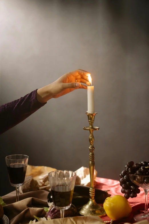 a woman lighting a candle on top of a table, by Leo Michelson, pexels, renaissance, studio photo, pouring, snacks, dramatic lighting”