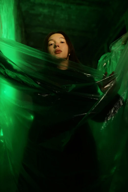 a woman in a dark room with a green light, an album cover, unsplash, conceptual art, dressed in plastic bags, gongbi, inflatable, wearing black clothes and cape