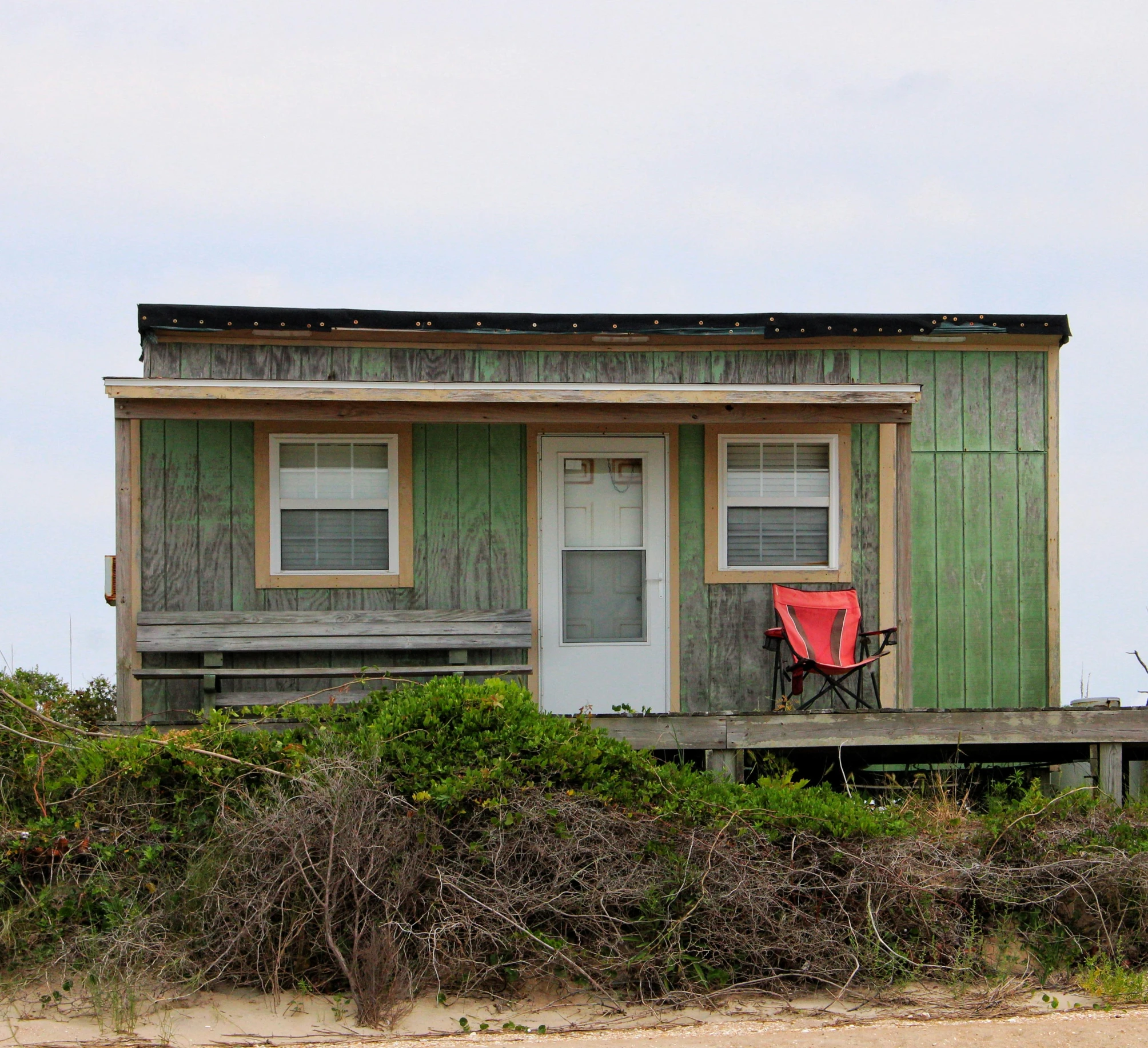 a green house sitting on top of a sandy beach, a portrait, tiny house, weathered, with a front porch, image