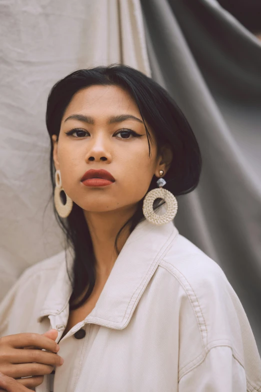 a woman wearing a white jacket and earrings, inspired by Ruth Jên, trending on pexels, sumatraism, portrait of modern darna, looking towards camera, lê long, young woman