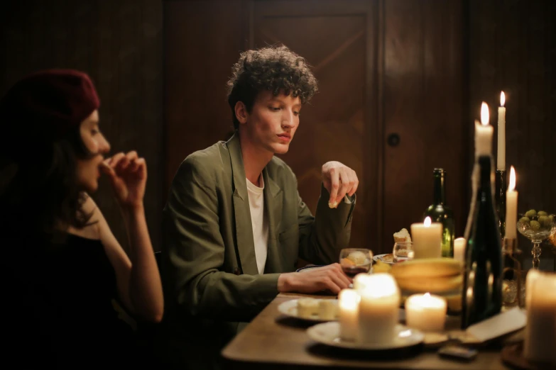 a man and a woman sitting at a dinner table, inspired by Nan Goldin, pexels, renaissance, finn wolfhard, in a room full of candles, androgynous male, on wooden table