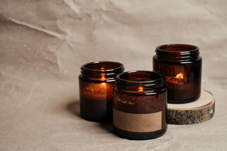 three candles sitting next to each other on a table, pexels, minimalism, glass jar, brown resin, sustainable, manuka