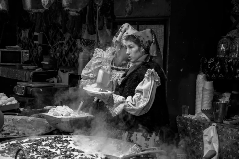 a black and white photo of a woman preparing food, a black and white photo, by Kristian Zahrtmann, renaissance, wearing victorian rags, dry ice, the vibrant echoes of the market, elaborate costume