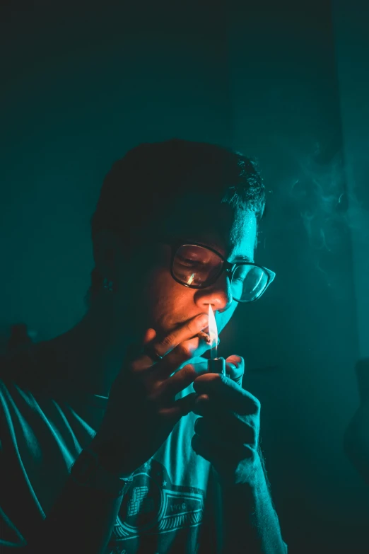 a man smoking a cigarette in a dark room, inspired by Elsa Bleda, pexels contest winner, man with glasses, ganja, teal aesthetic, blue and green light