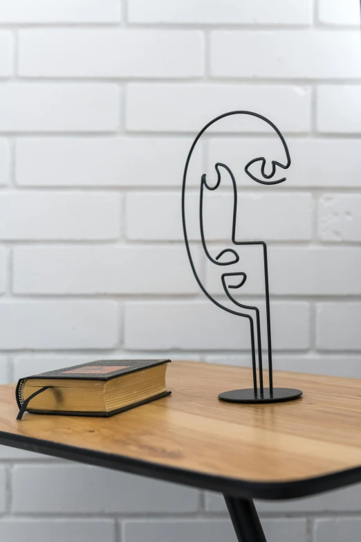 a book sitting on top of a table next to a lamp, an abstract sculpture, inspired by Alexander Archipenko, unsplash, side profile portrait, made of wire, standing on a shelf, face shown