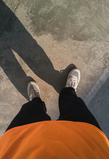 a person standing next to a skateboard on a sidewalk, inspired by Cheng Jiasui, high shadow, orange grey white, running shoes, 8k selfie photograph
