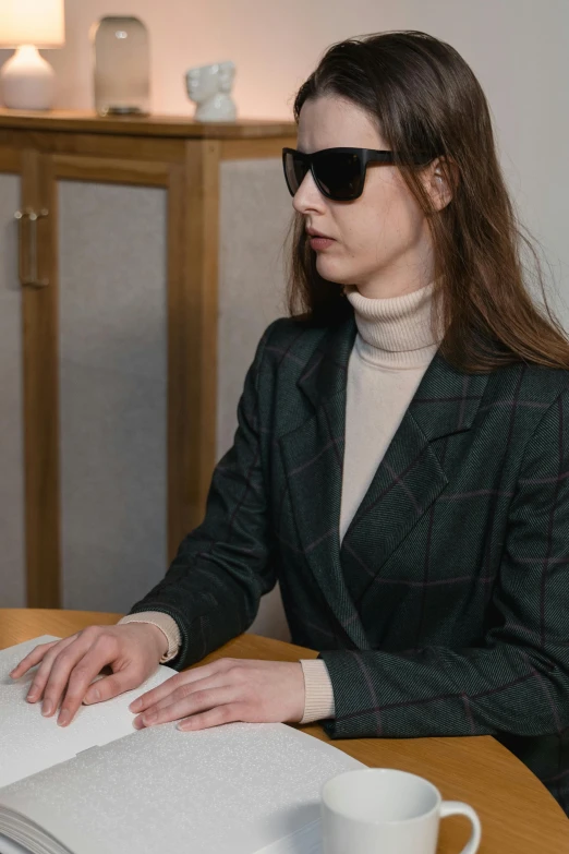 a woman sitting at a table in front of a laptop computer, an album cover, by Emma Andijewska, trending on unsplash, visual art, subject detail: wearing a suit, wearing shades, russian academic, lie detector test