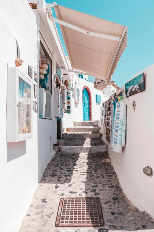 a narrow street with white buildings and blue doors, a photo, street art, crafts and souvenirs, ocean view, shops, small steps leading down