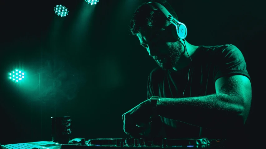 a man standing in front of a laptop with headphones on, by Sebastian Vrancx, pexels, process art, stage at a club, dark teal lighting, avatar image, green lights