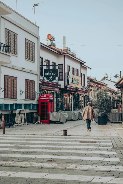 a man walking across a street next to tall buildings, a picture, trending on unsplash, art nouveau, cyprus, ground level view of soviet town, pub, preserved historical