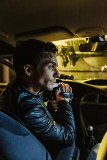 a man sitting in a car talking on a cell phone, robert sheehan, strobe and laser lights, leather clothing, dash cam