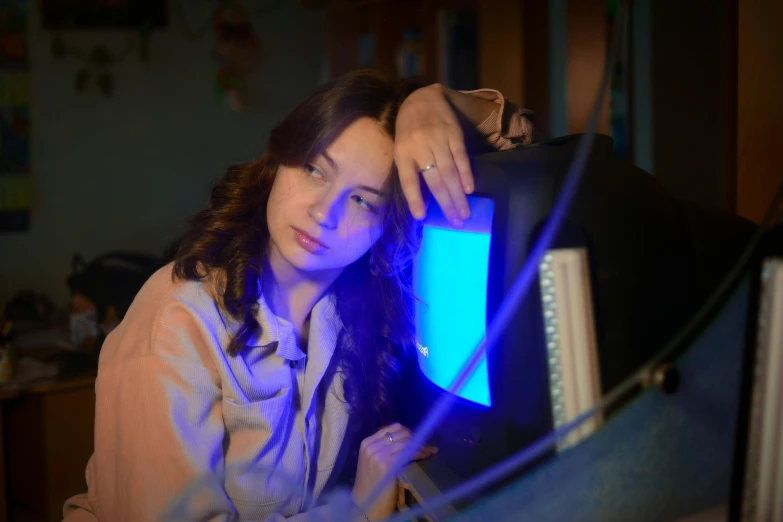 a woman sitting in front of a computer monitor, a portrait, inspired by Elsa Bleda, pexels, blue rays from tv, holding up a night lamp, sad look, sovietwave