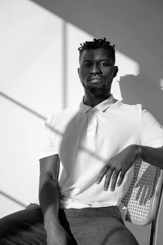 a black and white photo of a man sitting on a chair, inspired by Paul Georges, dark skin tone, sun behind him, maria borges, an all white human