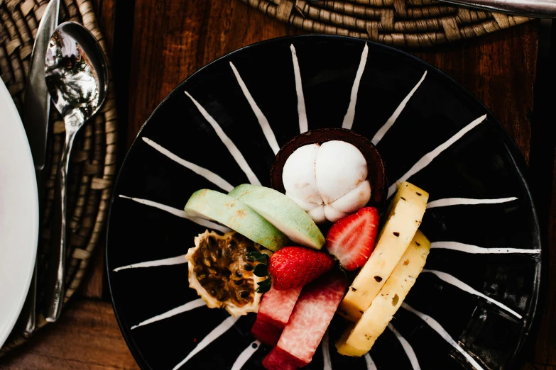 a close up of a plate of food on a table, a still life, unsplash, tropical fruit, background image, sitting on a mocha-colored table, black