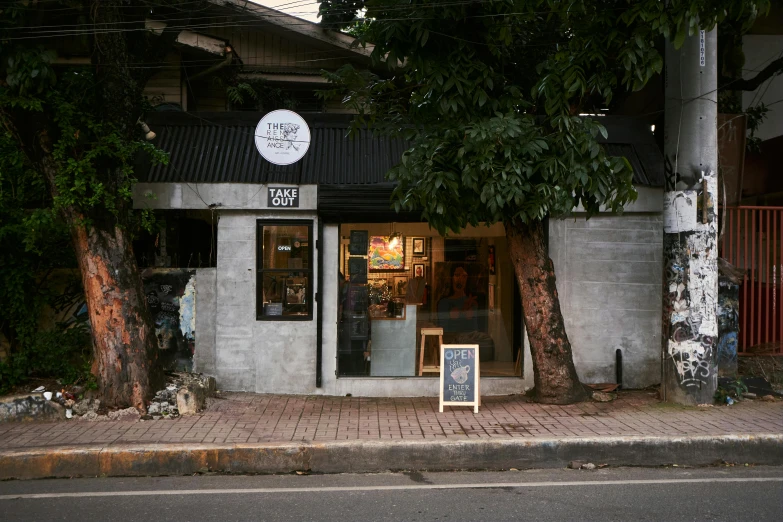 a building that has a sign in front of it, a portrait, temporary art, celebration of coffee products, batik, trees around, closed limbo room