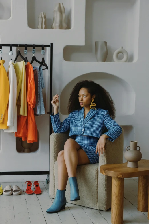 a woman sitting in a chair in front of a rack of clothes, blue and yellow theme, ashteroth, thumbnail, commercial