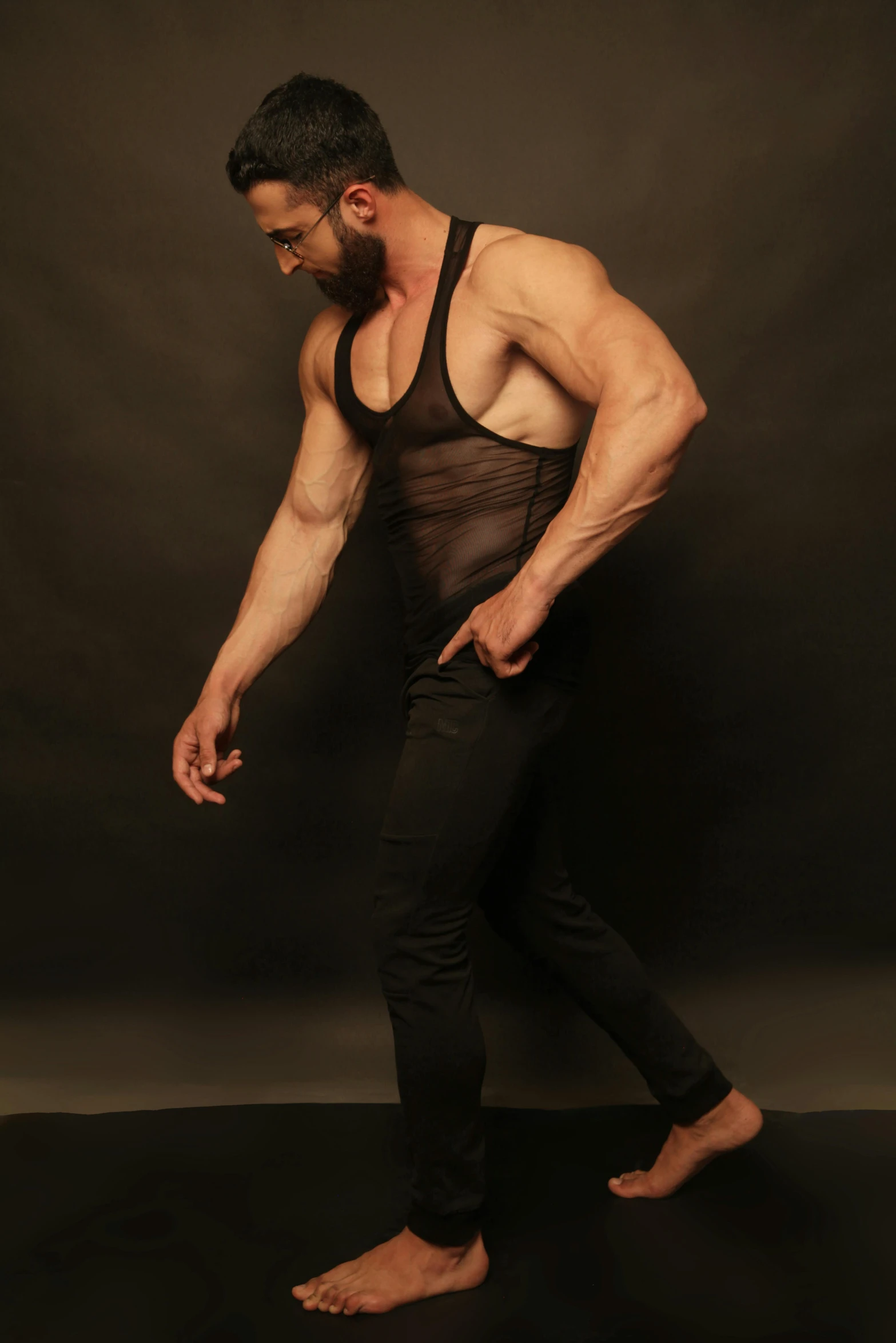 a man standing in front of a black background, by Andrew Stevovich, wearing : tanktop, fullbodysuit, mesh shirt, fit pic