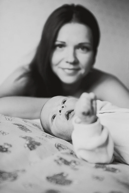 a woman laying on top of a bed next to a baby, a black and white photo, by Felix-Kelly, anna nikonova aka newmilky, high quality upload, finger, beautiful realistic photo