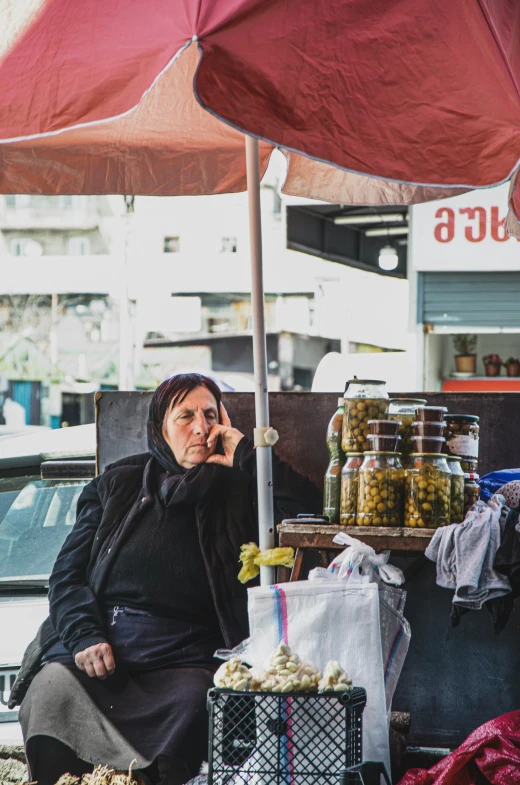 a woman sitting under an umbrella talking on a cell phone, a photo, by Ibrahim Kodra, olives, middle eastern style vendors, portrait featured on unsplash, chile